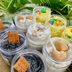 A beautiful top-down view of various whipped soaps, including Charcoal Coffee with a chocolate bar soap embed and others with heart-shaped embeds. The texture is just dreamy.