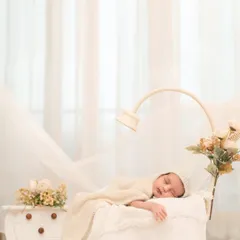 A vertical composition focusing on the sleeping baby, wrapped snugly in a basket. The flowing white curtains in the background add a soft, dreamy quality to this classic baby portrait.