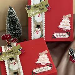 Making Christmas magical with personalized gift boxes. These bright red boxes are decorated with snowman ribbons and custom name tags for Ellora and Arya.