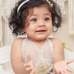 A beautiful close-up of a baby with curly hair and an expressive face. The simple boho theme with a macrame backdrop adds a touch of natural elegance.