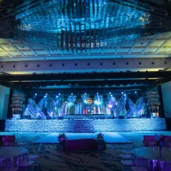 A full view of our modern, iridescent Sangeet stage. The design features a textured, shimmering facade, large-scale abstract leaf structures with integrated lighting, and a massive LED screen backdrop, all coming together to create a high-energy, concert-like atmosphere.