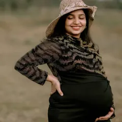 A solo maternity portrait capturing the pure happiness of a mother-to-be. Her joyful smile and the natural, open field setting create a sense of peace and contentment. The simple hat adds a touch of timeless style.