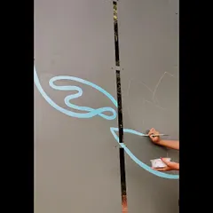 The beginning stages of a new mural. Here, you can see my hand sketching out the initial design and painting the first light blue outlines on a large grey panel.