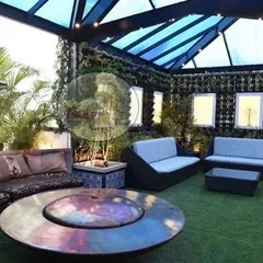 This covered lounge area shows how we create all-weather outdoor living spaces. The large, curved sofa is centered around a fire pit table, under a translucent pergola roof that provides shelter without blocking natural light. Vertical gardens enclose the space for privacy.