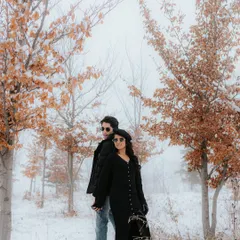 A moody, atmospheric shot of a couple standing back-to-back amidst snow-dusted trees in Azerbaijan. The fog and autumn leaves add a touch of mystery and romance to their pre-wedding story.