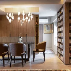 This dining area, part of the 'Library of Music' residence, is surrounded by floor-to-ceiling bookshelves. A modern, sculptural light fixture hangs above the dining table, creating an intimate and sophisticated space for meals and conversations.