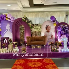We designed this royal princess theme for a first birthday, using a rich purple color palette. The stage includes multiple arched backdrops, a miniature sofa for photos, a light-up number '1', and a princess carriage prop, all set on a purple carpeted stage.