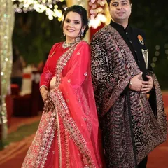 Here is a beautiful example of a coordinated reception look. The bride is wearing a stunning red velvet and net lehenga, while the groom complements her in a classic black sherwani paired with a detailed shawl.