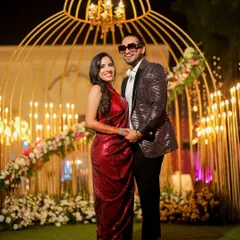 A classic portrait of a newly engaged couple. They stand before a stunning golden birdcage-like decor piece, holding hands and smiling, perfectly capturing the elegance of their engagement party.