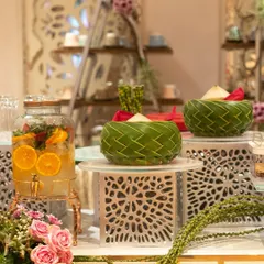 An elegant beverage station with a large glass dispenser of citrus-infused water and woven leaf bowls. The setup is both beautiful and functional, offering guests a refreshing drink option.