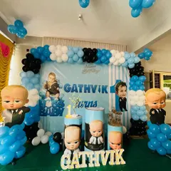 A Boss Baby themed first birthday party in a hall. This setup uses a large backdrop with character graphics, multiple Boss Baby cutouts on balloon pillars, and the birthday boy's name in wooden letters.