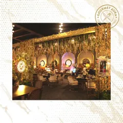 A wide view of a lavish event space we catered, featuring lush floral arrangements and our signature neon logo. We create an immersive brand experience.