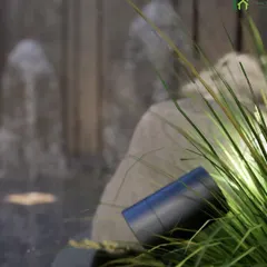 A detail shot of our landscape lighting. An adjustable spotlight is strategically placed within the greenery to highlight the texture of plants and cast a gentle glow on a nearby water feature, enhancing the garden's nighttime beauty.