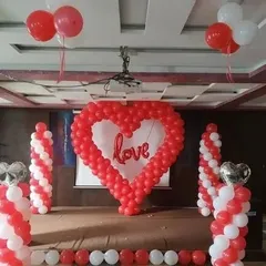 This stage decoration is perfect for an engagement party or anniversary celebration. It features a large heart-shaped balloon sculpture as the centerpiece, framed by red and white spiral balloon pillars for a classic romantic look.