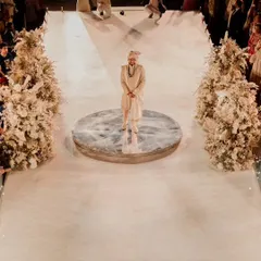The groom stands on a mirrored platform at the start of the aisle, awaiting his bride. The aisle is lined with what looks like a forest of white florals, creating a dramatic and ethereal path.