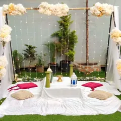 A serene white-themed picnic setup for two. This arrangement includes a backdrop of draped fabric and fairy lights, with small teepees and pampas grass adding to the calm, bohemian aesthetic.