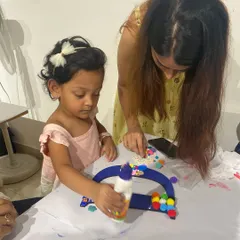A mother helps her little girl decorate a monogram letter with colorful pom-poms. These moments of shared creativity between parents and children are what make our studio so special.