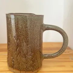 This tall, hand-built mug has a subtle wheat pattern pressed into the clay, giving it a lovely texture. The earthy brown glaze makes it a warm and rustic addition to any kitchen.