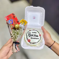 Our signature Rakhi combo, held and ready for gifting. It includes a "Happy Raksha Bandhan" bento cake and a mini bouquet with a Ferrero Rocher and Dairy Milk, perfect for the occasion.