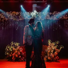 A dramatic, cinematic shot of the couple on stage, surrounded by flowers and spotlights. This is the kind of epic Sangeet portrait we specialize in.