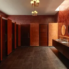 The women's restroom at Samavana is designed to be an experience in itself. The deep red textured walls, dramatic lighting, and row of circular mirrors create a bold and luxurious space.