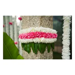 A stone pillar is wrapped with a thick band of white and pink chrysanthemums over a base of sacred mango leaves, a classic detail in traditional South Indian decor.