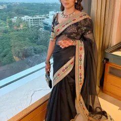 The client poses by a window, the natural light highlighting her glowing makeup and the saree's intricate border.