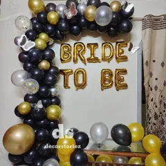 A classic 'BRIDE TO BE' decor setup perfect for a bachelorette party or bridal shower at home. We used a black, gold, and silver balloon arch and large gold foil letters to create this fun and celebratory photo backdrop.