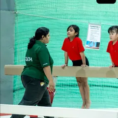 A coach provides guidance to a young gymnast on the balance beam. Our program emphasizes safety and proper technique from the very first lesson.