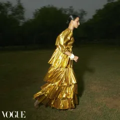 An editorial for Vogue that captures movement and drama. The styling features a tiered, metallic gold dress that creates a fluid, sculptural shape as the model moves, blending high fashion with a sense of dynamic energy.