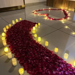 A beautiful pathway of red rose petals leading to a heart shape on the floor. The path is lined with battery-operated candles for a safe and romantic glow.
