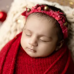 A close-up of a newborn in our Christmas setup, with a festive red headband and twinkling lights in the background.
