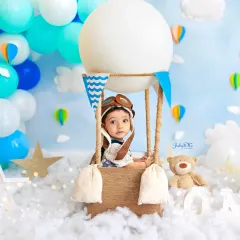 This little aviator is peeking out from his hot air balloon, ready for an adventure in the clouds. The pilot hat and dreamy blue backdrop create a magical scene for a one-year milestone session.