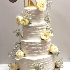 Simple elegance is timeless. This four-tiered wedding cake is finished with textured whipped cream and adorned with fresh white roses and baby's breath, proving that a classic design can be the most beautiful centerpiece for your special day.