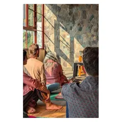 Sunlight streams into the meditation hall, casting shadows across the natural stone wall. This image captures the interplay of light, texture, and human presence that brings the space to life.