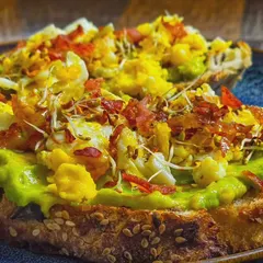 A close-up of the delicious layers on our avocado toast. You can see the creamy avocado, fluffy eggs, and crispy bacon.