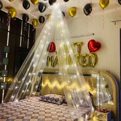 A 'Just Married' first-night room decoration. I use a canopy of sheer fabric and fairy lights over the bed, with gold and black balloons on the ceiling and 'Just Married' foil letters on the wall.