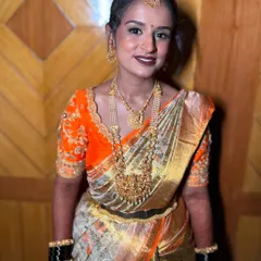 A classic South Indian bridal look. The combination of a bright orange and gold saree, layered temple necklaces, and a neat hair bun creates a look of timeless tradition.