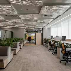 A flexible workspace with booth seating and hot desks, featuring patterned acoustic ceiling panels. The design incorporates planters to divide the space and improve air quality, creating a productive and healthy environment.