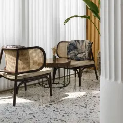 This quiet seating nook features dark wood rattan chairs against a backdrop of sheer white curtains, creating a soft, diffused light. It’s an intimate corner perfect for conversation, combining classic materials with modern comfort.