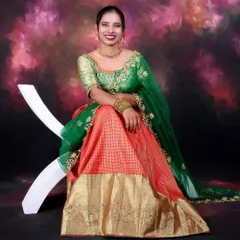 A vibrant solo portrait of a woman in beautiful traditional attire. The studio lighting makes the colors of the green and orange dress pop against the painted backdrop.