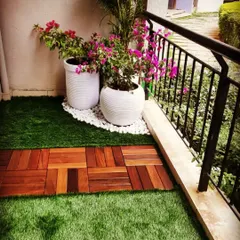 A practical and beautiful flooring solution. I created a pathway using wooden deck tiles through a field of soft artificial grass, leading to a corner decorated with flowering plants in modern white planters.