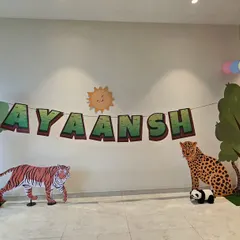A cute and simple jungle-themed backdrop for Ayaansh's first birthday. The setup includes tree and animal cutouts like a tiger, leopard, and bear, with a personalized name banner.