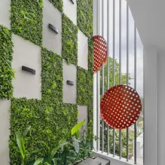 The triple-height courtyard acts as a balcony garden attached to the living room, extending the space outdoors. The vertical garden and perforated red metal discs create a visual delight accessible from every floor.