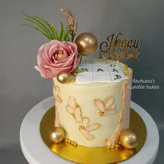 A moist chocolate cake decorated with a pink rose, golden spheres, and butterfly accents.