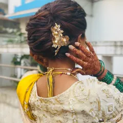 A close-up of a textured bridal bun, finished with a delicate golden floral accessory. This style adds a modern touch to the traditional khopa, with soft lines and a less rigid structure, perfect for an engagement or reception.