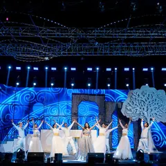 A performance featuring the bride with backup dancers. The choreography is designed to highlight the bride while the synchronized movements and props, like the large tree cutout, create a visually rich and cohesive stage picture.