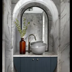 This powder room is a jewel box of design. A marble-clad arched niche perfectly frames the sculptural wash basin and mirror, while the fluted semi-circular vanity adds a touch of modern texture and artistry.