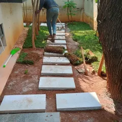 My team member is installing rolls of fresh grass turf around the newly laid stepping stones, carefully fitting them into place.