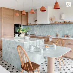 This view showcases the versatile kitchen island, which extends into a dining table. The combination of pastel blue tiles, wood cabinets, and terracotta pendant lights creates a warm, inviting look.